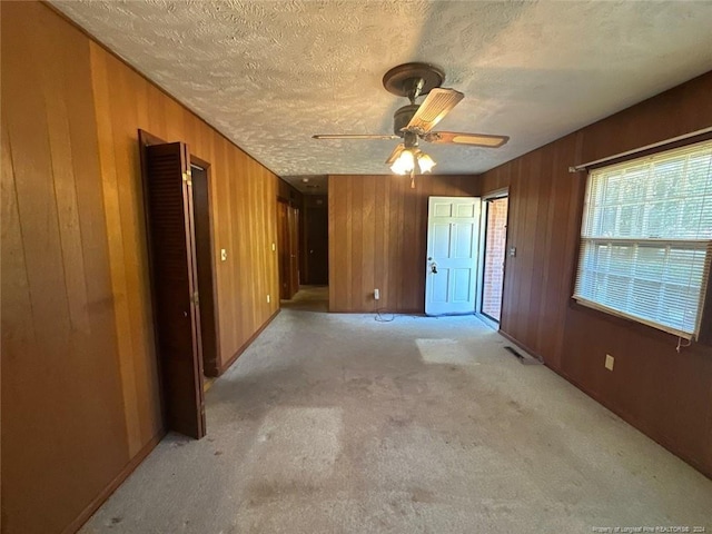 unfurnished room featuring ceiling fan, light colored carpet, a textured ceiling, and wooden walls