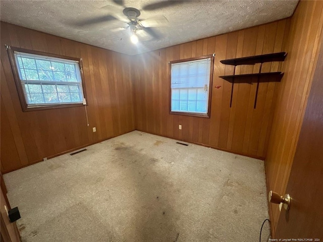 spare room featuring ceiling fan, light carpet, and wooden walls