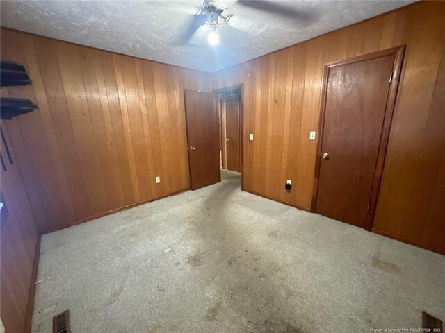 spare room with ceiling fan, light colored carpet, a textured ceiling, and wooden walls