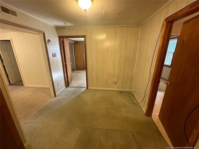 corridor with light carpet, wood walls, and a textured ceiling