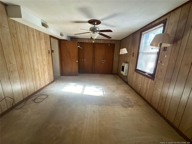 empty room featuring heating unit, ceiling fan, and wood walls