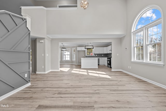 unfurnished living room with light hardwood / wood-style floors, a high ceiling, and a chandelier