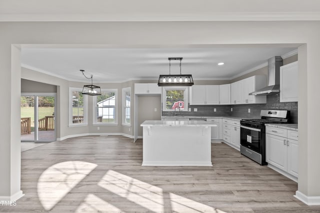 kitchen featuring white cabinets, stainless steel range, wall chimney exhaust hood, and plenty of natural light