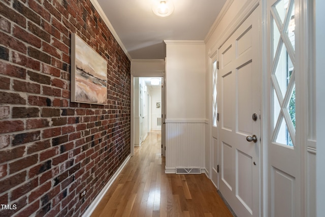 hallway featuring light hardwood / wood-style floors, ornamental molding, and brick wall