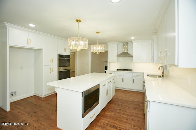 kitchen with stainless steel appliances, sink, wall chimney range hood, a center island, and white cabinetry