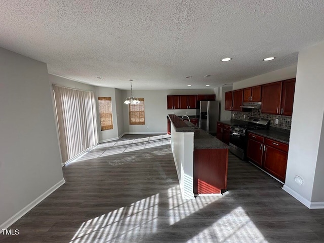 kitchen featuring dark hardwood / wood-style floors, an island with sink, a chandelier, pendant lighting, and appliances with stainless steel finishes