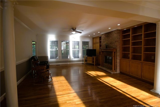 unfurnished living room with ceiling fan, dark wood-type flooring, a brick fireplace, decorative columns, and crown molding