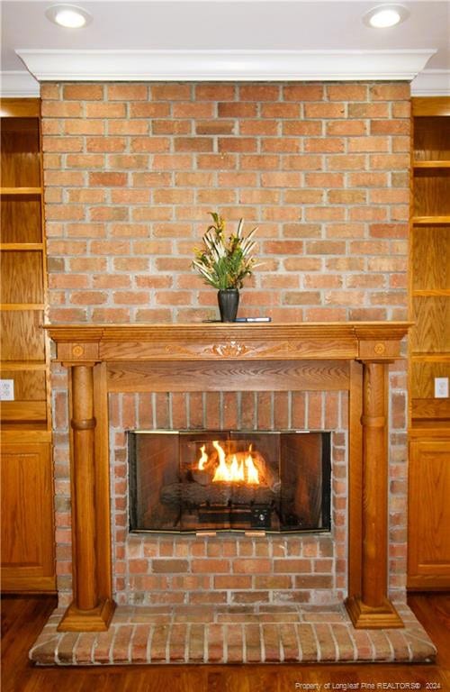 interior details with built in shelves, ornamental molding, wood-type flooring, and a brick fireplace