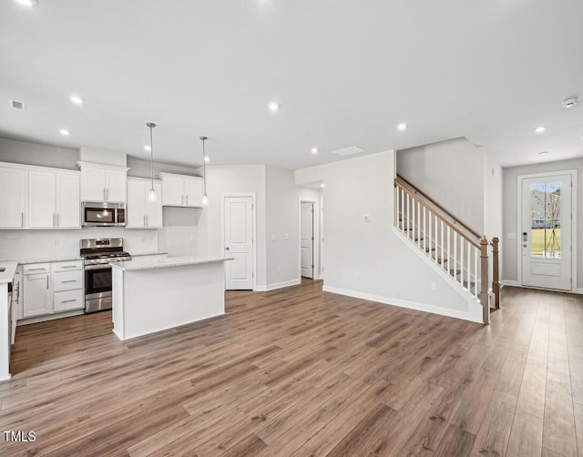 kitchen with a center island, stainless steel appliances, decorative light fixtures, white cabinets, and light wood-type flooring