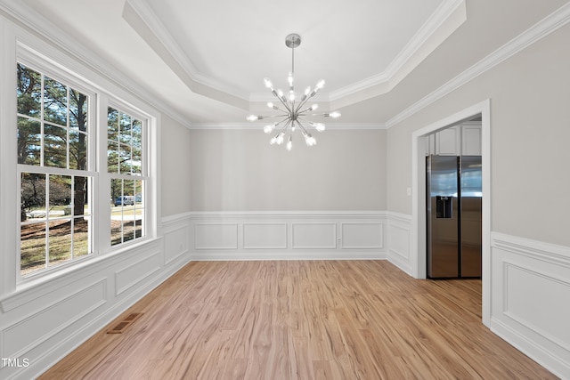 unfurnished dining area featuring a raised ceiling, an inviting chandelier, light hardwood / wood-style flooring, and ornamental molding