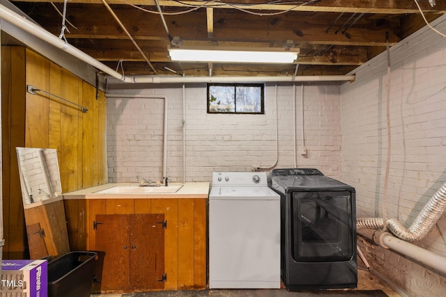 laundry area with brick wall, washer and clothes dryer, and sink