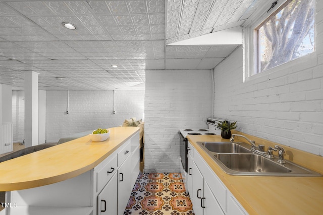 kitchen with range with electric cooktop, brick wall, white cabinetry, sink, and light tile patterned floors