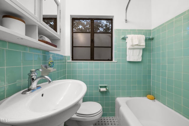 bathroom with tile walls, sink, toilet, and a tub to relax in