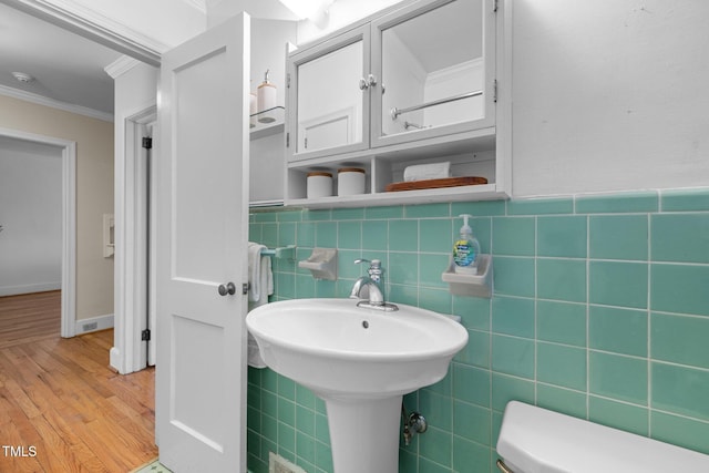 bathroom with ornamental molding, wood-type flooring, tile walls, and toilet