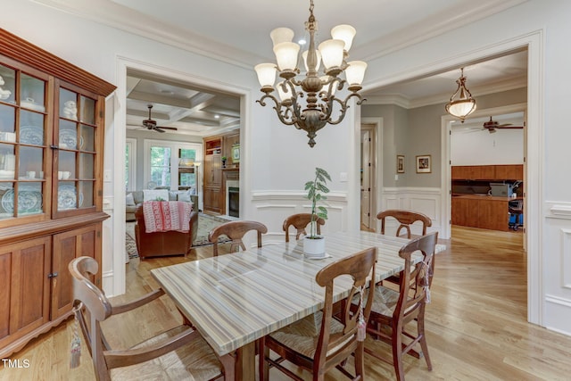 dining room featuring light wood-type flooring, beam ceiling, ceiling fan with notable chandelier, ornamental molding, and coffered ceiling