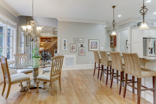 dining room featuring sink, light hardwood / wood-style flooring, ornamental molding, and an inviting chandelier