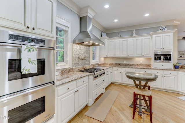 kitchen featuring white cabinets, light hardwood / wood-style floors, wall chimney range hood, and appliances with stainless steel finishes