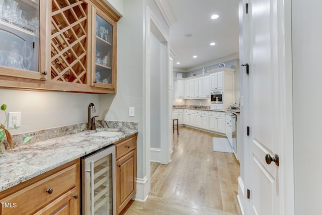 bar with light stone countertops, white cabinets, beverage cooler, sink, and light wood-type flooring