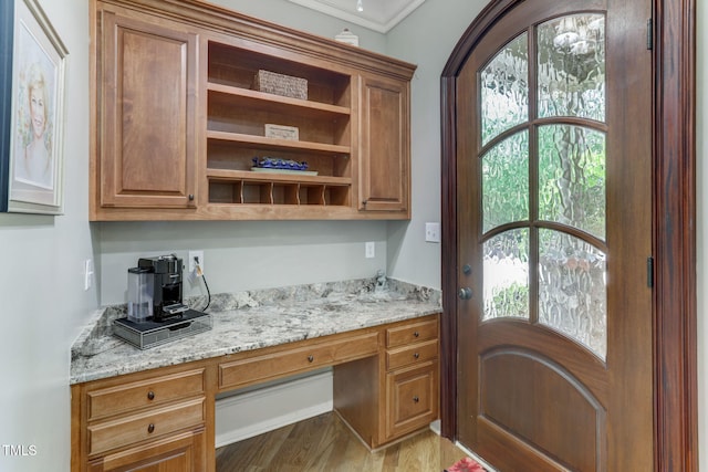 bar with crown molding, a healthy amount of sunlight, light stone countertops, and built in desk