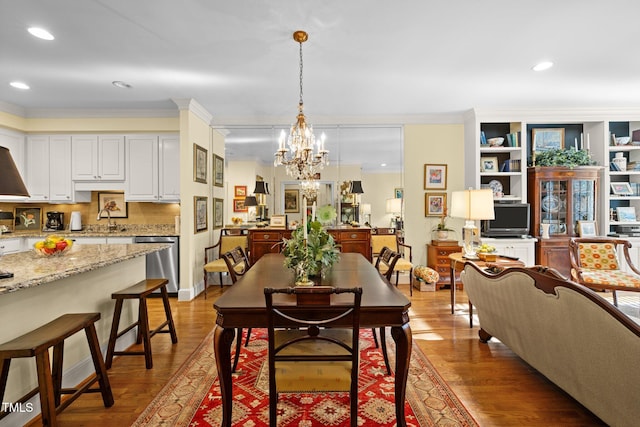 dining area with crown molding, wood-type flooring, sink, and a chandelier