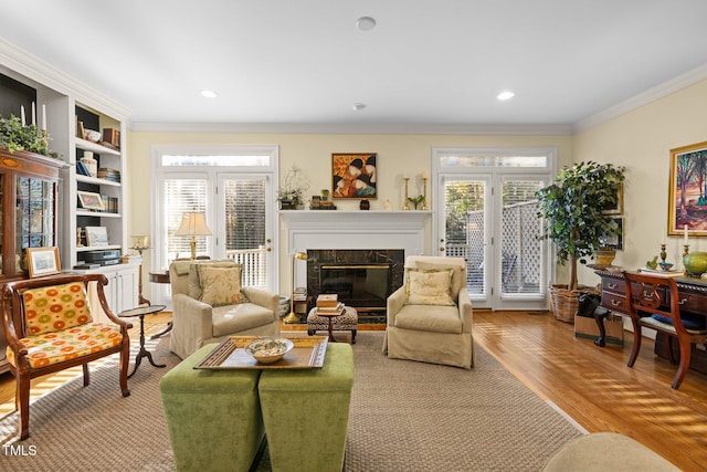 living area featuring built in features, light hardwood / wood-style flooring, crown molding, and a premium fireplace