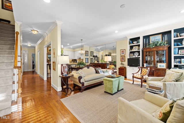 living room with built in features, wood-type flooring, ornamental molding, and an inviting chandelier