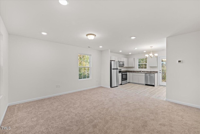 unfurnished living room with a wealth of natural light, sink, light colored carpet, and a notable chandelier