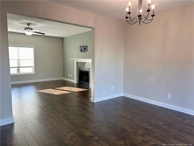 unfurnished living room with ceiling fan with notable chandelier and dark hardwood / wood-style flooring