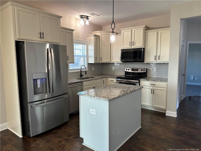 kitchen with appliances with stainless steel finishes, light stone counters, sink, decorative light fixtures, and a kitchen island