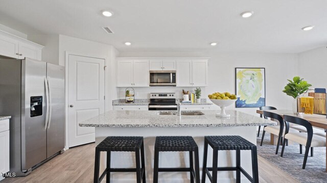 kitchen featuring light hardwood / wood-style floors, white cabinetry, a kitchen island with sink, and appliances with stainless steel finishes