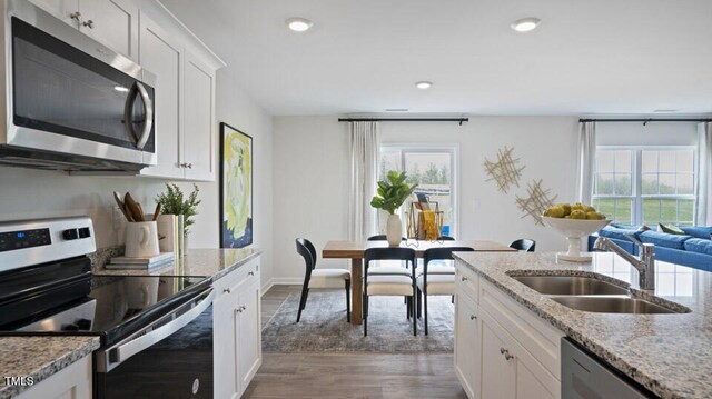 kitchen with appliances with stainless steel finishes, light stone counters, sink, white cabinets, and hardwood / wood-style floors