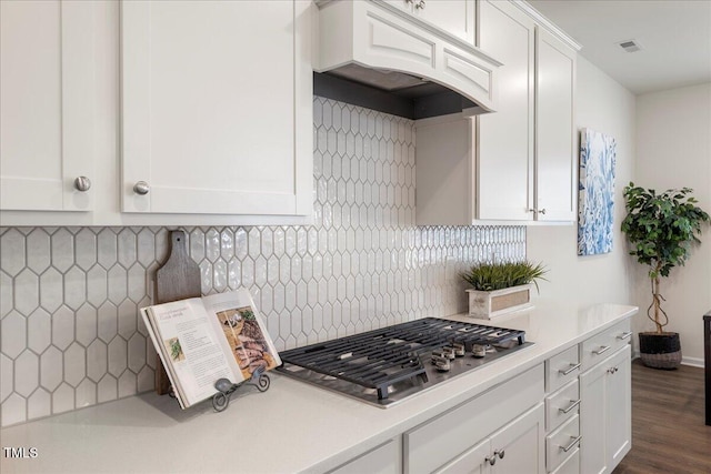 kitchen with white cabinetry, dark wood-type flooring, stainless steel gas cooktop, tasteful backsplash, and custom range hood