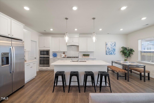 kitchen with white cabinetry, stainless steel appliances, dark hardwood / wood-style floors, decorative light fixtures, and a center island with sink