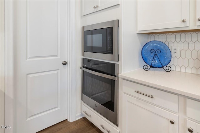 kitchen with stainless steel oven, backsplash, dark hardwood / wood-style floors, built in microwave, and white cabinetry