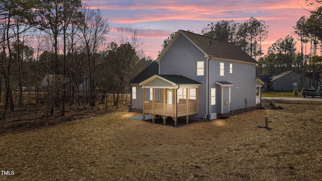 back house at dusk with a sunroom and a yard