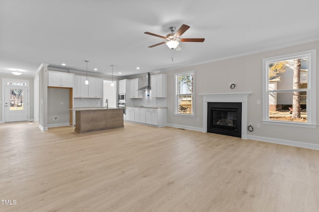 unfurnished living room featuring sink, ornamental molding, light hardwood / wood-style floors, and ceiling fan