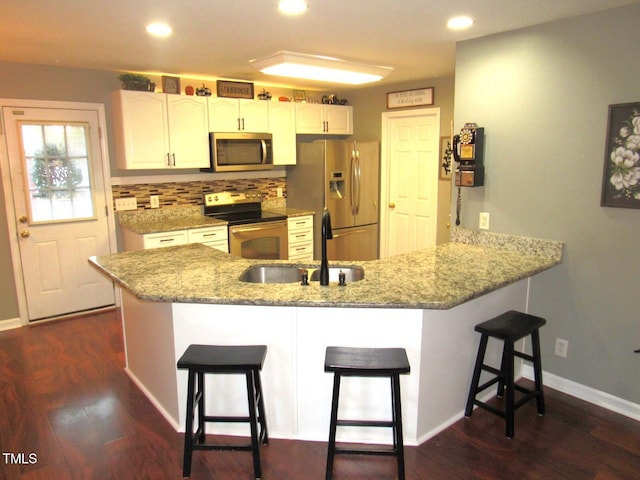 kitchen with dark wood-type flooring, stainless steel appliances, kitchen peninsula, a breakfast bar area, and white cabinets