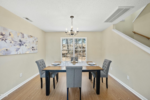 dining area featuring a textured ceiling, light hardwood / wood-style flooring, and a notable chandelier