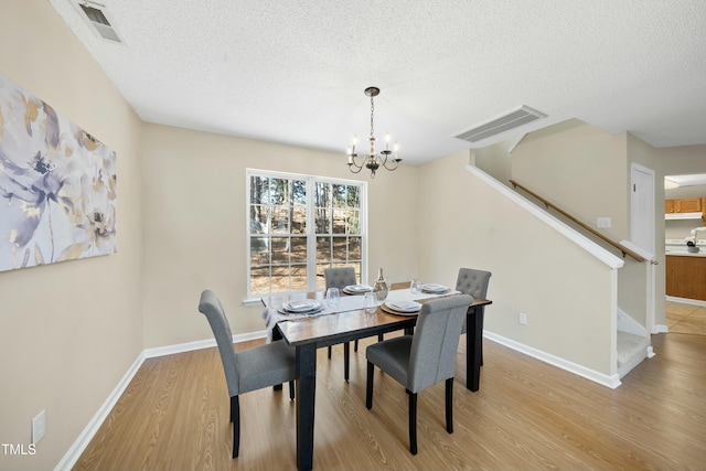 dining space with an inviting chandelier, a textured ceiling, and light hardwood / wood-style floors