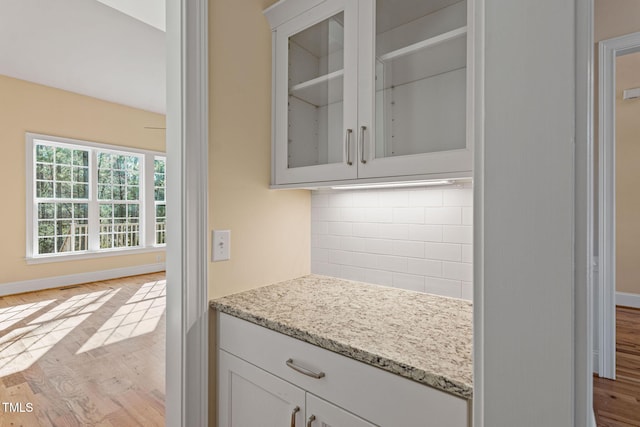 kitchen featuring white cabinets, light hardwood / wood-style floors, backsplash, and light stone countertops