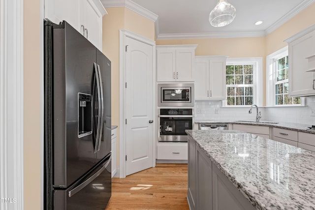 kitchen featuring light stone counters, hanging light fixtures, stainless steel appliances, white cabinetry, and sink