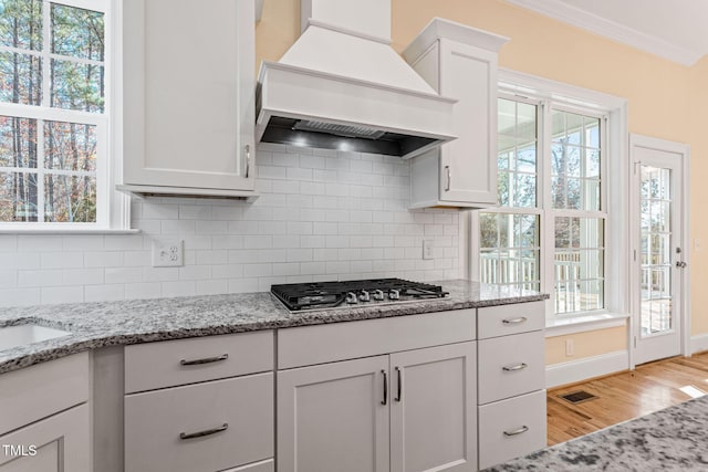 kitchen featuring light stone counters, premium range hood, tasteful backsplash, stainless steel gas stovetop, and white cabinets