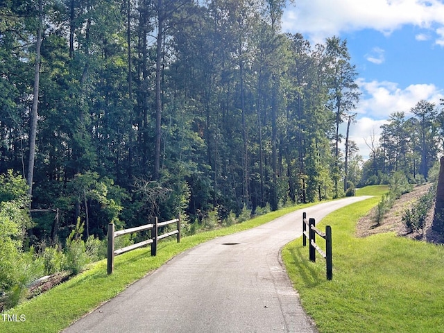 surrounding community with aphalt driveway, a yard, fence, and a forest view