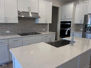 kitchen with backsplash, white cabinets, a sink, under cabinet range hood, and black appliances