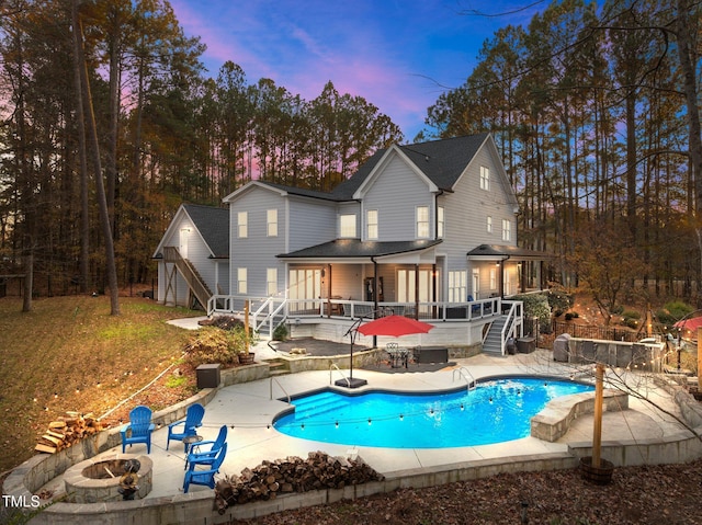 back house at dusk featuring a fire pit, a pool side deck, and a patio