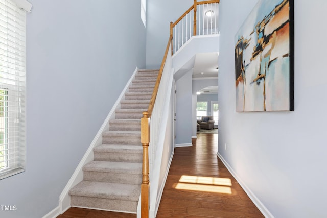 stairway featuring baseboards, arched walkways, a high ceiling, and wood finished floors
