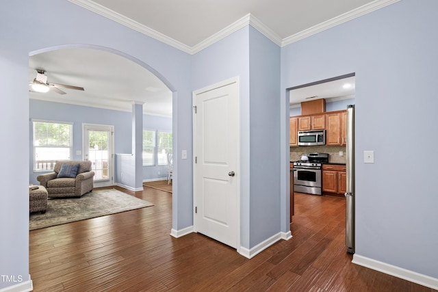 entryway featuring crown molding, a ceiling fan, baseboards, dark wood-type flooring, and arched walkways
