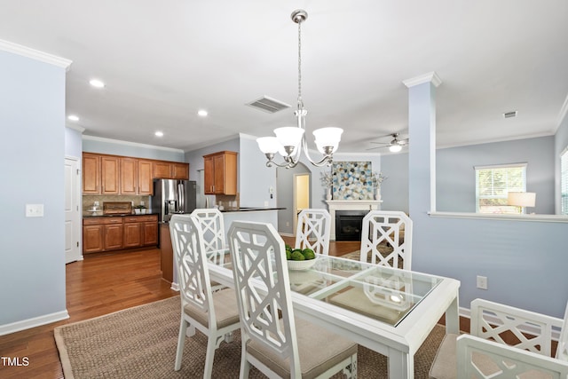 dining area featuring visible vents, ornamental molding, wood finished floors, and ceiling fan with notable chandelier