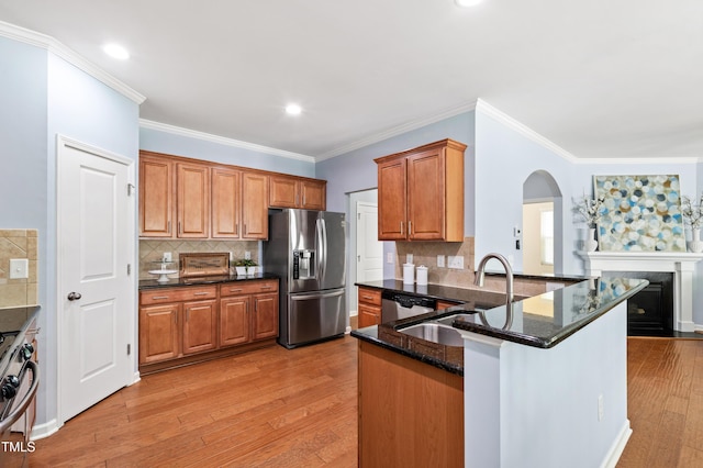 kitchen with arched walkways, a sink, dark stone countertops, light wood finished floors, and stainless steel appliances