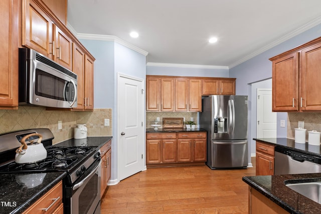 kitchen featuring backsplash, crown molding, appliances with stainless steel finishes, dark stone countertops, and light wood-style floors